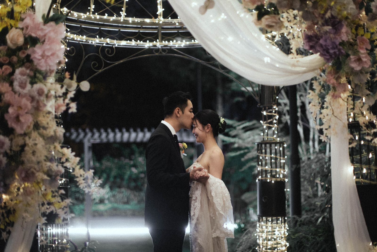 Couple sharing a kiss under the floral gazebo at a night garden wedding at The Summerhouse