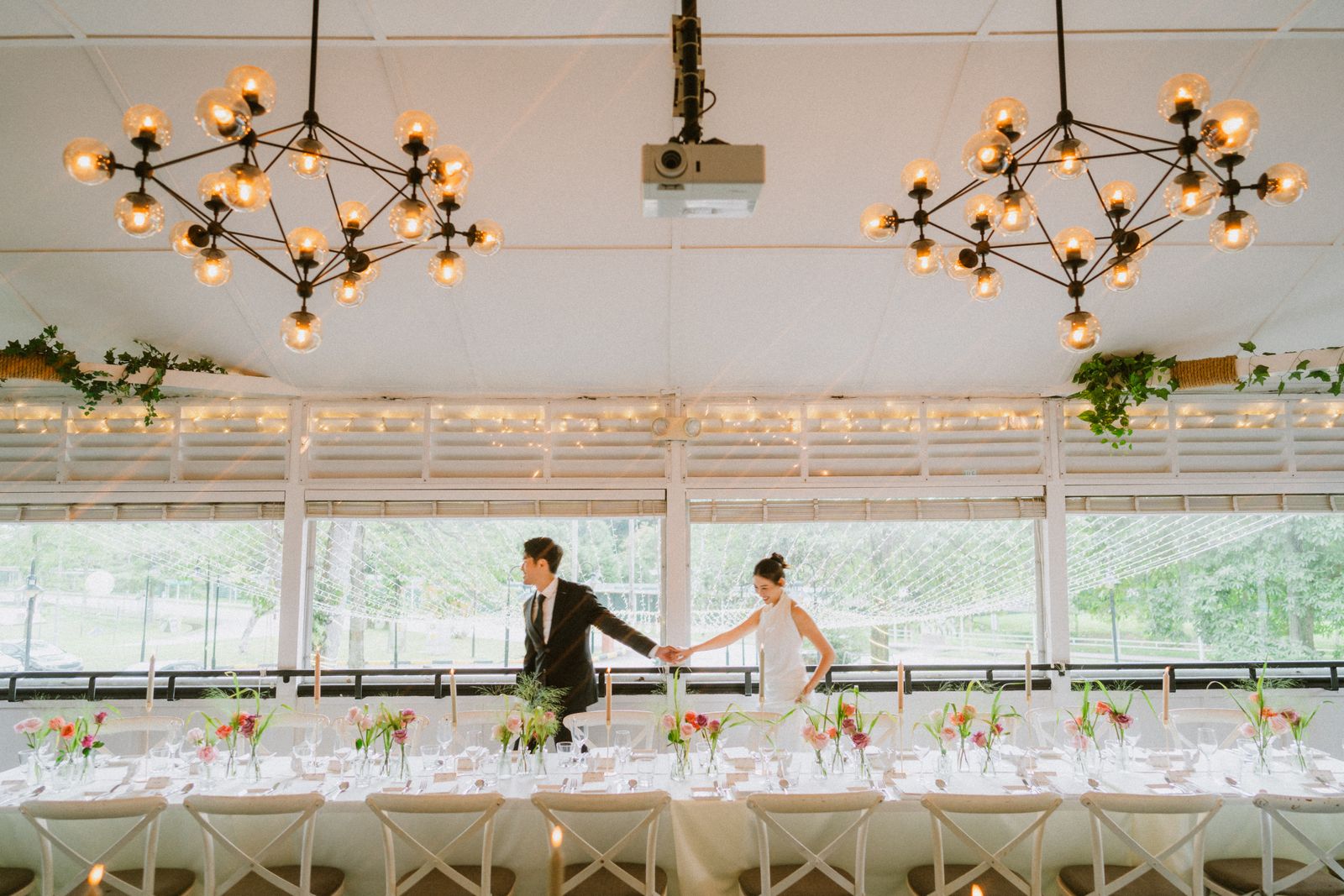 Newlyweds walking past the reception table under glowing chandeliers at The Summerhouse